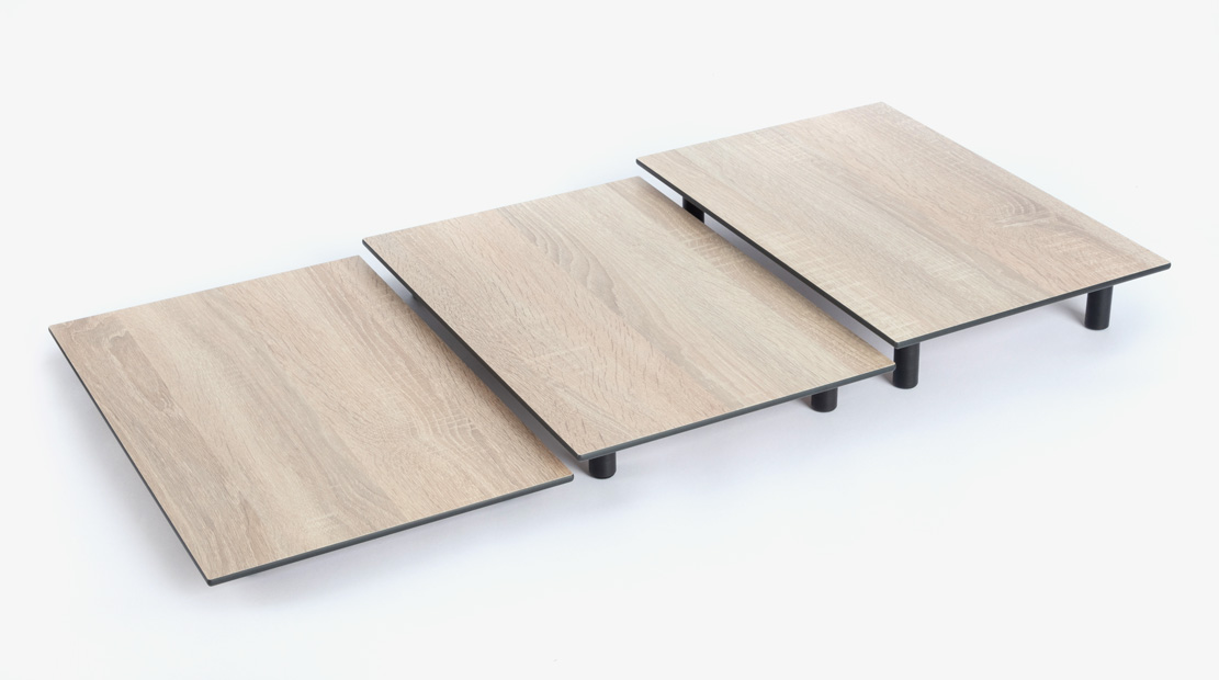 Drei rechteckige Holzplatten auf schwarzen Füßen, stufenförmig angeordnet